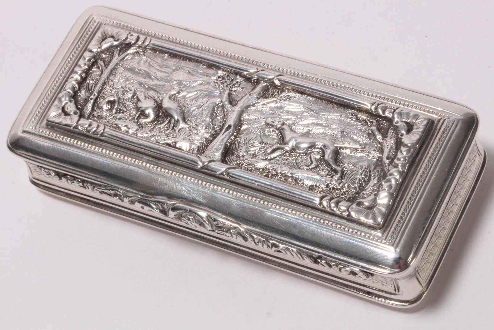 Good George IV Sterling Silver Snuff Box and Cover: hallmarked London, 1825, John Jones III, of narrow rectangular form, set with a cast panel to cover displaying hunting dog and birds in a wooded landscape, above a foliate thumb piece opening to gilt 