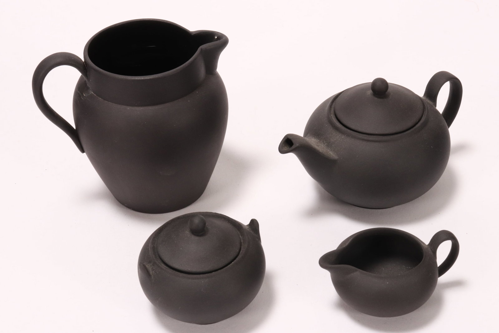 Wedgwood Black Basalt Miniature Tea Set,: comprising tea pot, twin handled sugar bowl and creamer, impressed Wedgwood//Made in England to base, together with a black basalt creamer, impressed Wedgwood//Made in England to base, height 6.5cm (4
