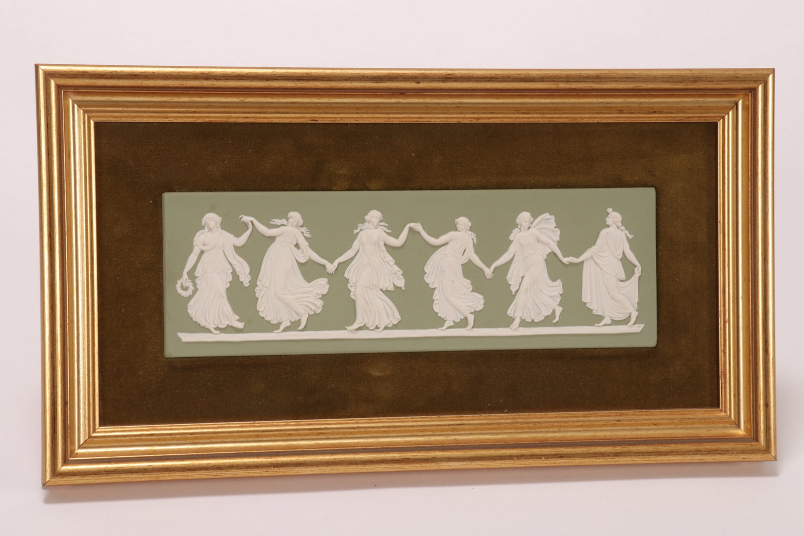 Wedgwood Jasperware 'Dancing Hours' Plaque,: of rectangular form, in white on sage green, impressed Wedgwood//Made in England to base, 7.5cm x 22.5cm, set on a green velvet ground in gilt frame, 18cm x 33cm