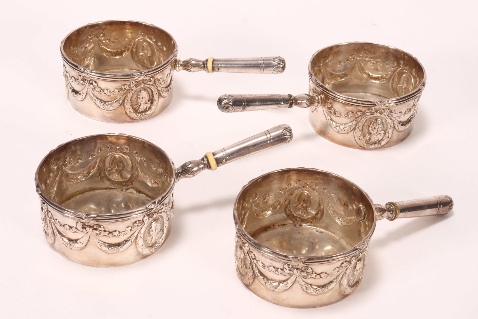 Set of Four German Silver Brandy Warmers,: with cylindrical bowl embossed with medallion portrait and swags, with tapering handle and insulator, total weight 252g, a/f to one, length 12cm (4)