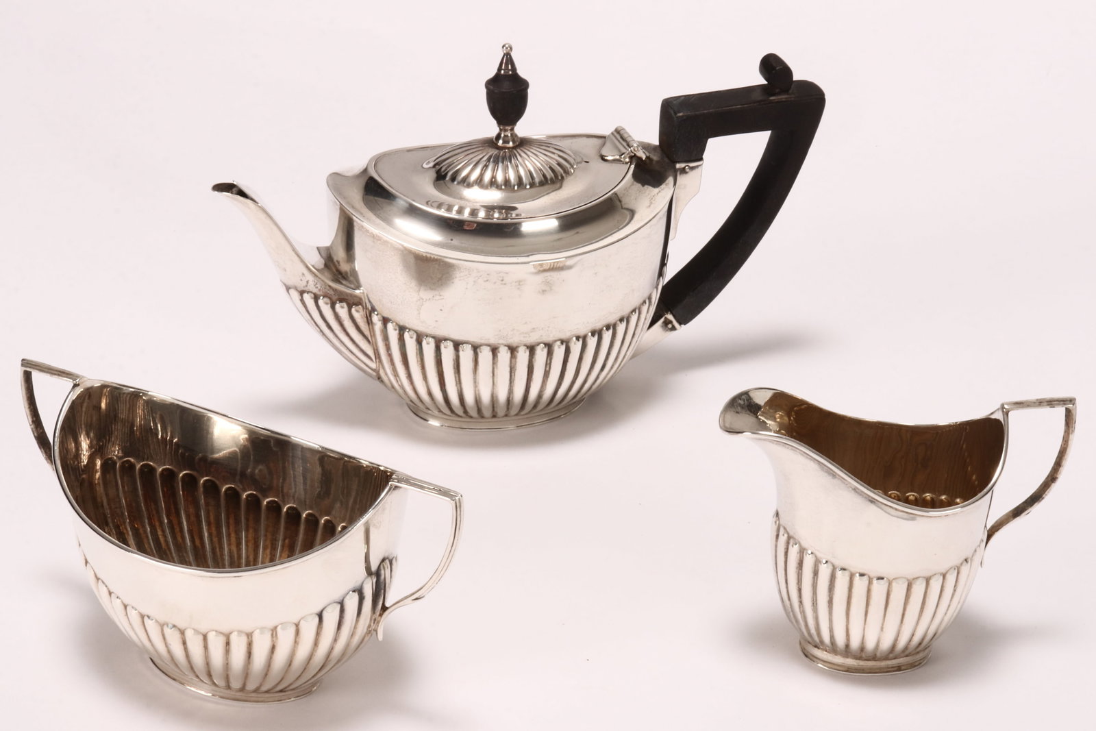 Late Victorian Sterling Silver Bachelor's Tea Set,: hallmarked London, 1898, William Hutton & Sons Ltd, comprising teapot, twin handled sugar bowl and creamer, the teapot with hinged domed cover set with wooden urn finial, each with a lobed lower body 