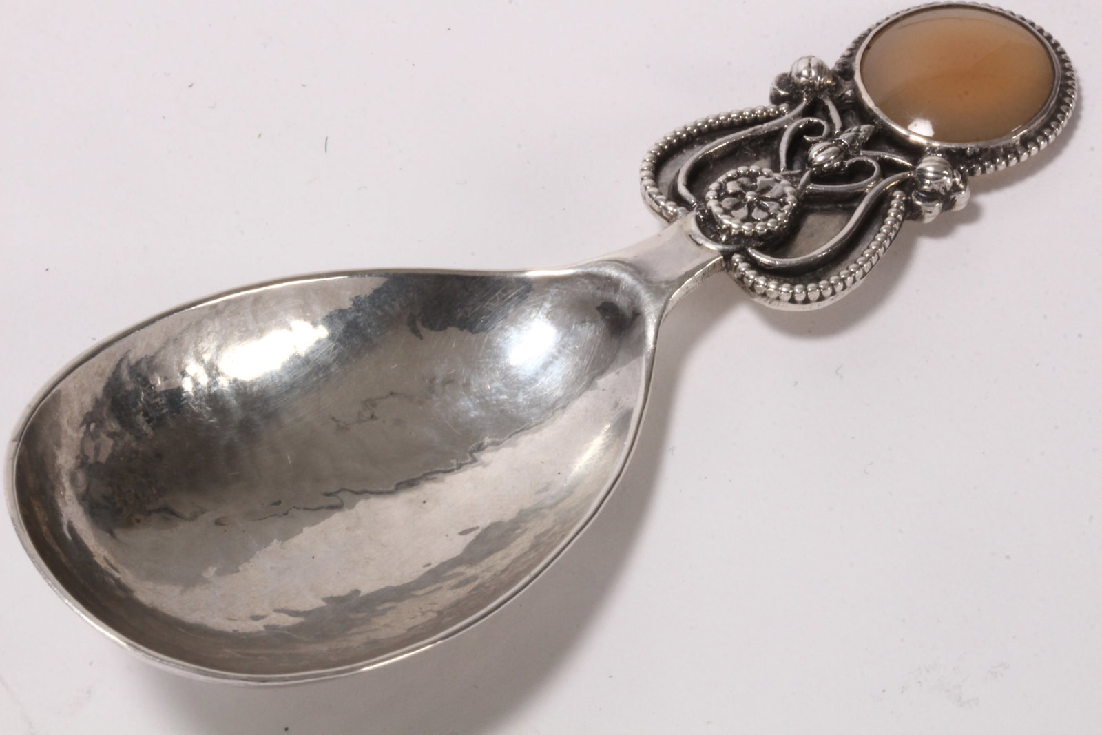 Arts and Crafts Sterling Silver Caddy Spoon,: hallmarked London, 1926, Sybil Dunlop, set with chalcedony cabochon finial and pierced handle with beaded surround, above hand beaten bowl, total weight 24g, length 9.5cm