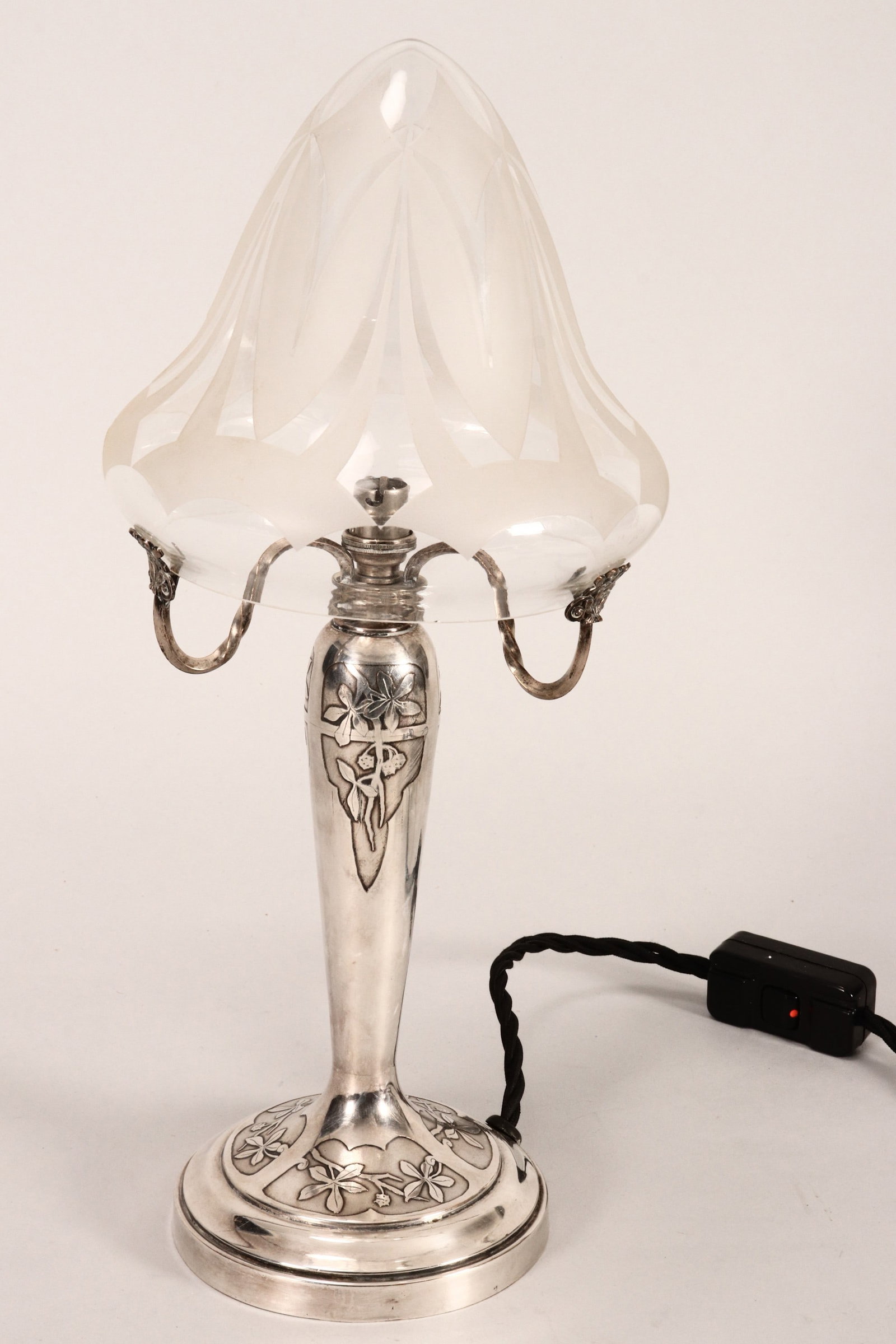 French Art Nouveau Table Lamp,: the silverplate base decorated in the Japanese taste with shaped cartouches containing blossoming branches, supporting a bell shaped acid etched shade, with Australian plug and switch, total height 38