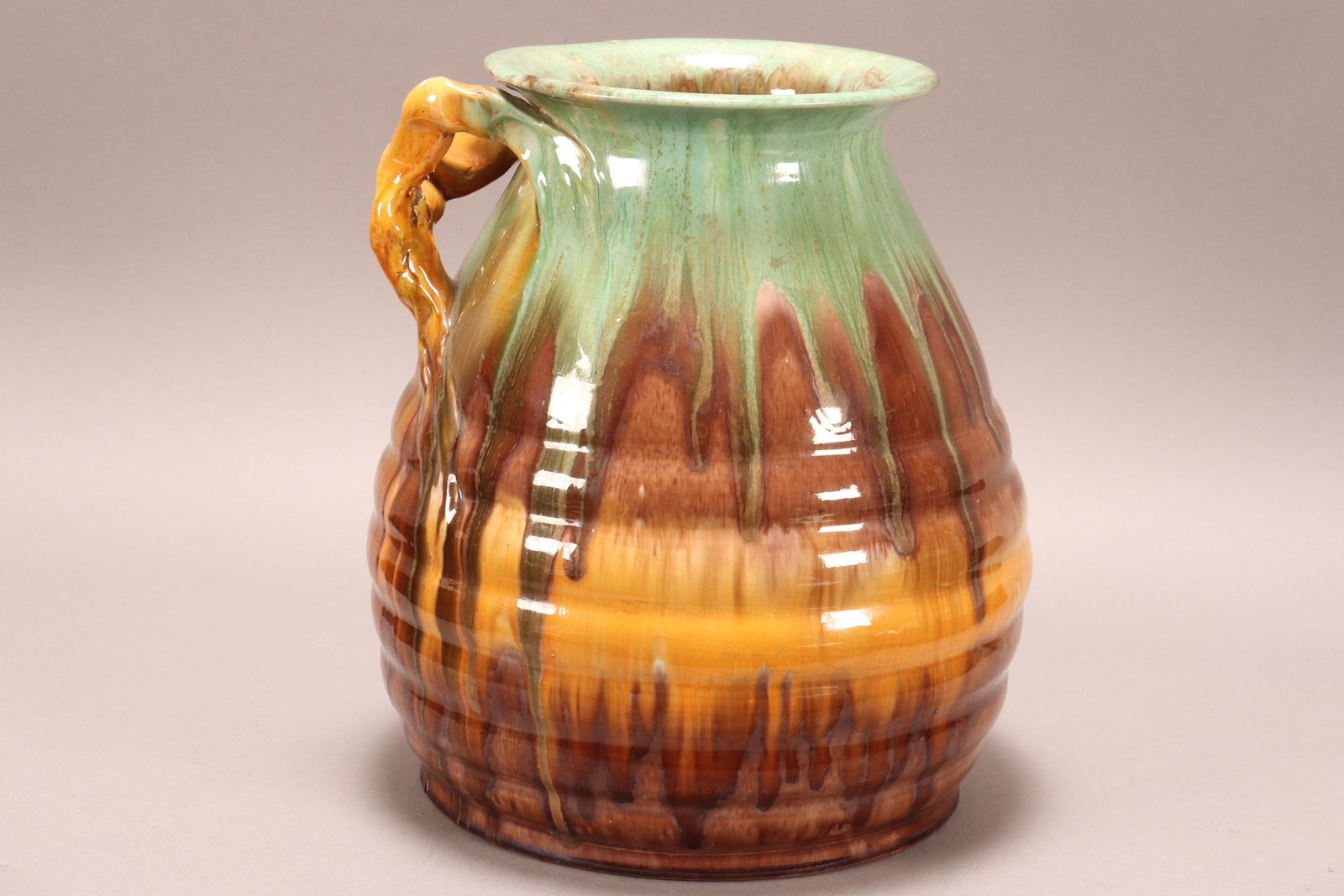 Large Australian Remued Pottery Vase,: of ribbed baluster form, set with a branched handle, in a green, amber and brown dribble glaze, signed verso and original label to body, a/f, height 27cm