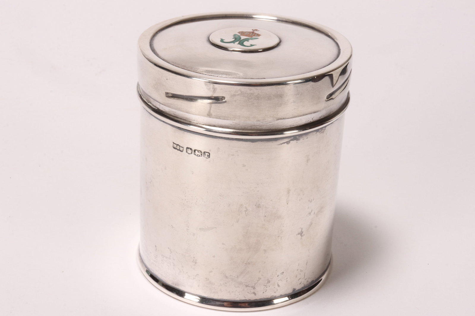George V Sterling Silver Lidded Box,: hallmarked Sheffield, 1934, M&W (Mappin & Webb), of cylindrical form, with cover decorated with enamel coat of arms depicting twin fish below a crown (possibly Lucknow), above a plain cylindrical body