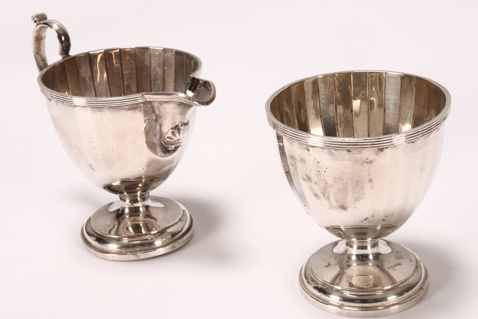 George V Sterling Silver Sugar Bowl and Creamer,: hallmarked Birmingham, 1926/27, Adie Bros., of deep facetted form with reeded rim, raised on a stepped circular foot, total weight 155g, height 7.5cm and 9cm (2)