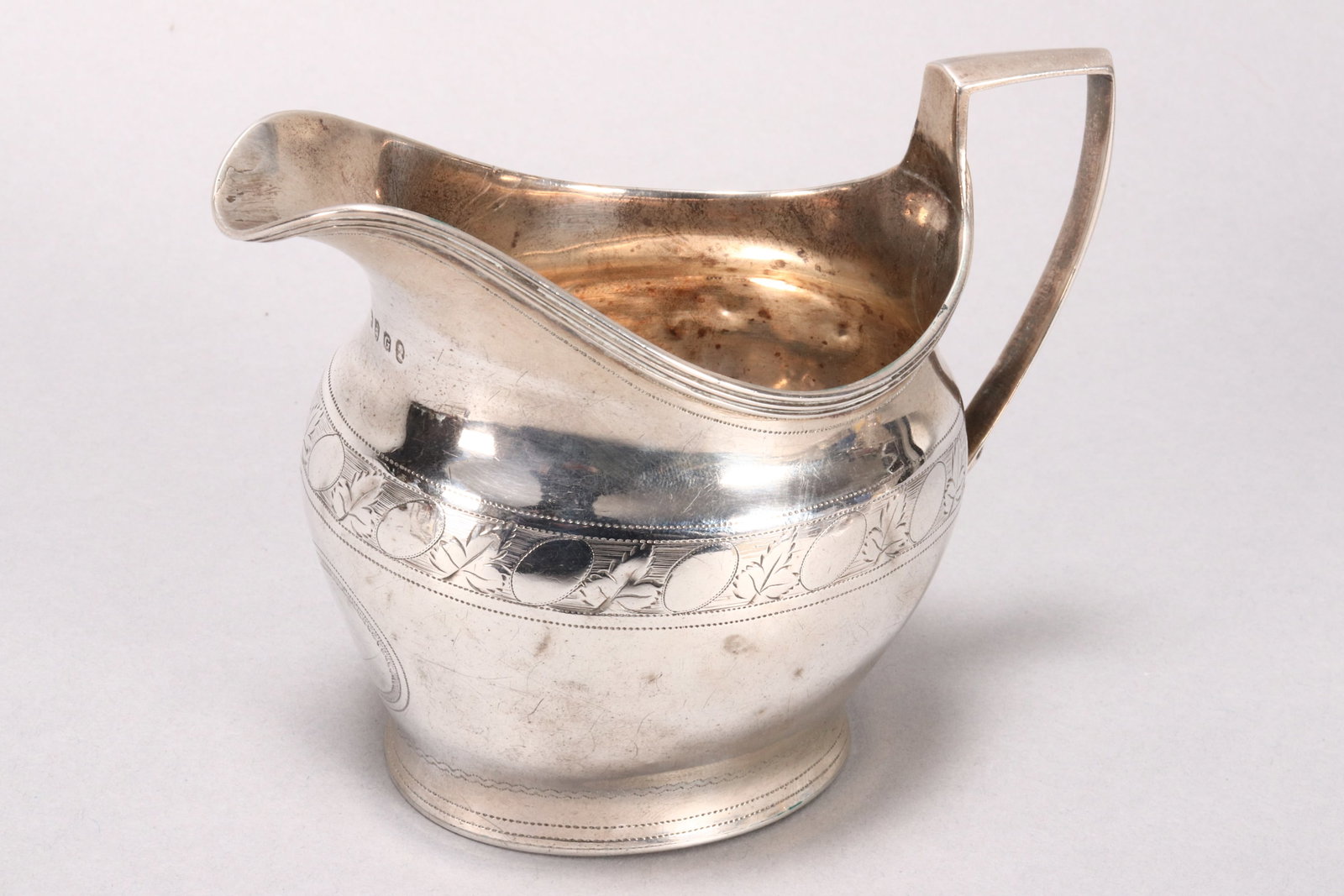 George III Sterling Silver Cream Jug,: hallmarked London, 1802, Solomon Hougham, with reeded edge and angled handle, above an oval baluster body engraved with frieze of leaf and oval motifs, the whole on a circular foot, a/f, total weight 