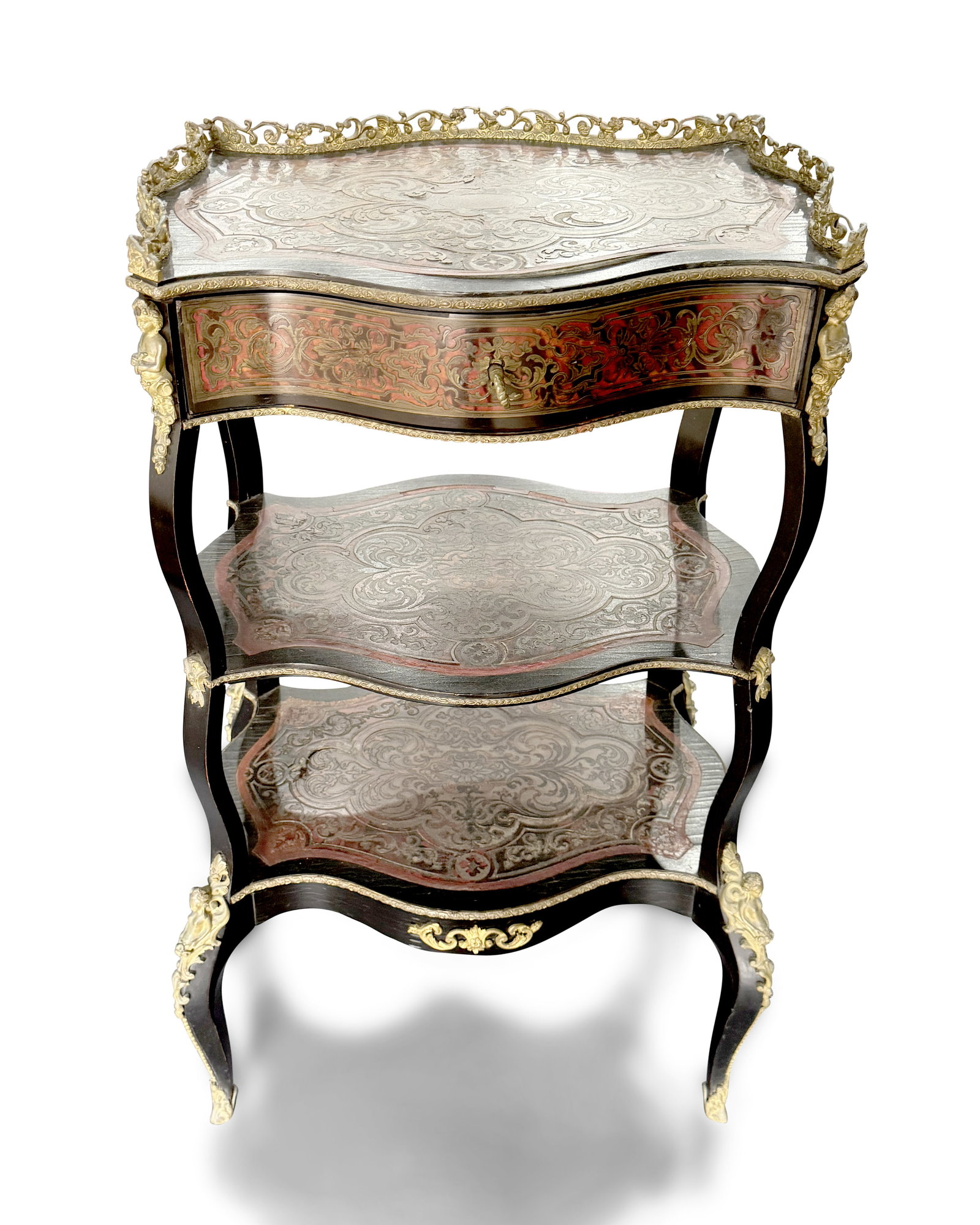 Victorian Boulle Style Three Tier What-Not,: with pierced brass gallery above a serpentine top, set with single drawer, raised on four shaped ebonised legs, with gilt brass figural accents, united by two lower shelves, with key, a/f (lifting to 