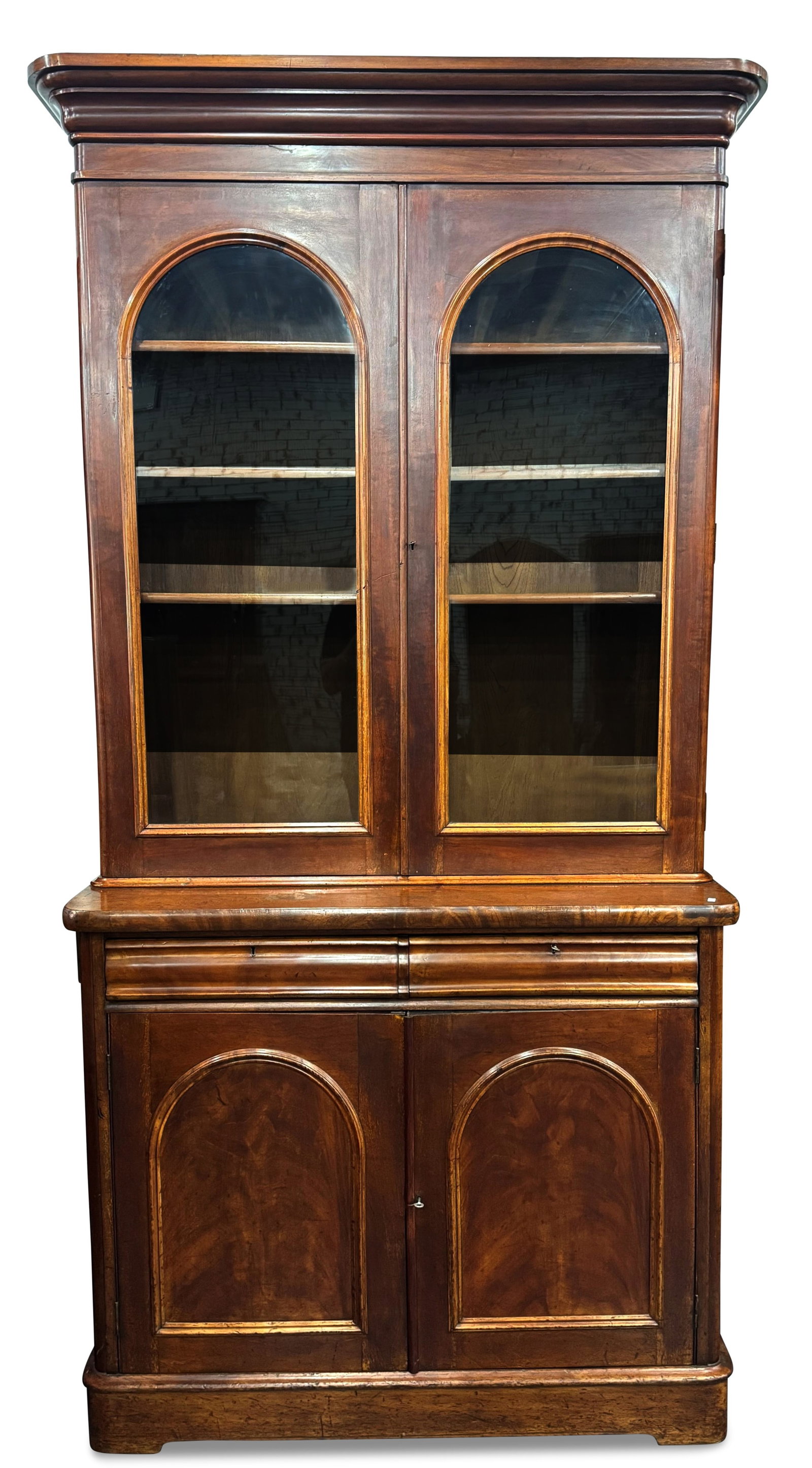 Victorian Cedar and Mahogany Bookcase,: of tall rectangular form, with molded pediment, above a pair of arched glass doors opening to shelves, above a pair of narrow pillow drawers, above a pair of arched panel doors, on a plinth base, 250c