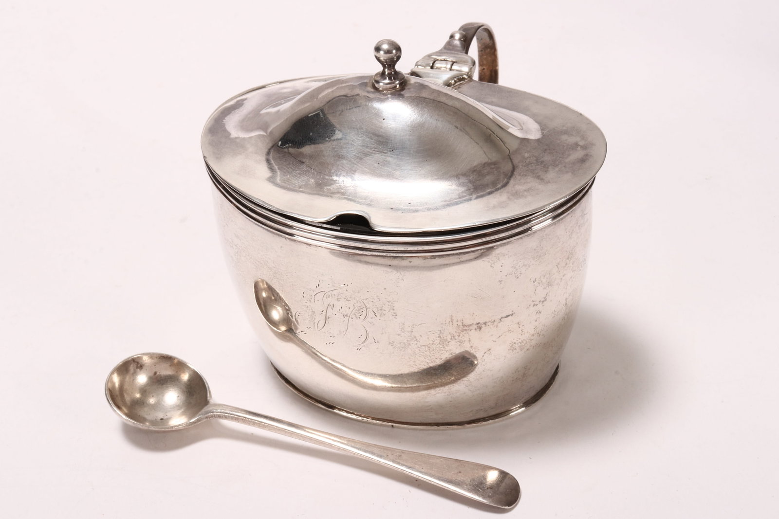 George III Sterling Silver Mustard Pot,: hallmarked London, 1800, makers mark rubbed, of navette form with hinged cover, accented with reeded borders and crest, with blue glass liner and later sterling silver mustard spoon, a/f, total weight