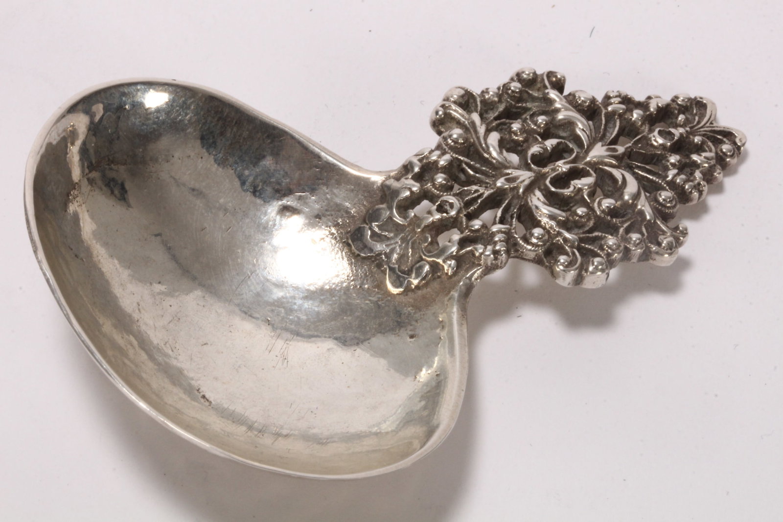 Art Nouveau Sterling Silver Caddy Spoon,: hallmarked London, 1919, Sandeim Brothers, with a pierced scrolled foliate handle, above a hand beaten oval bowl, total height 33cm, length 8cm