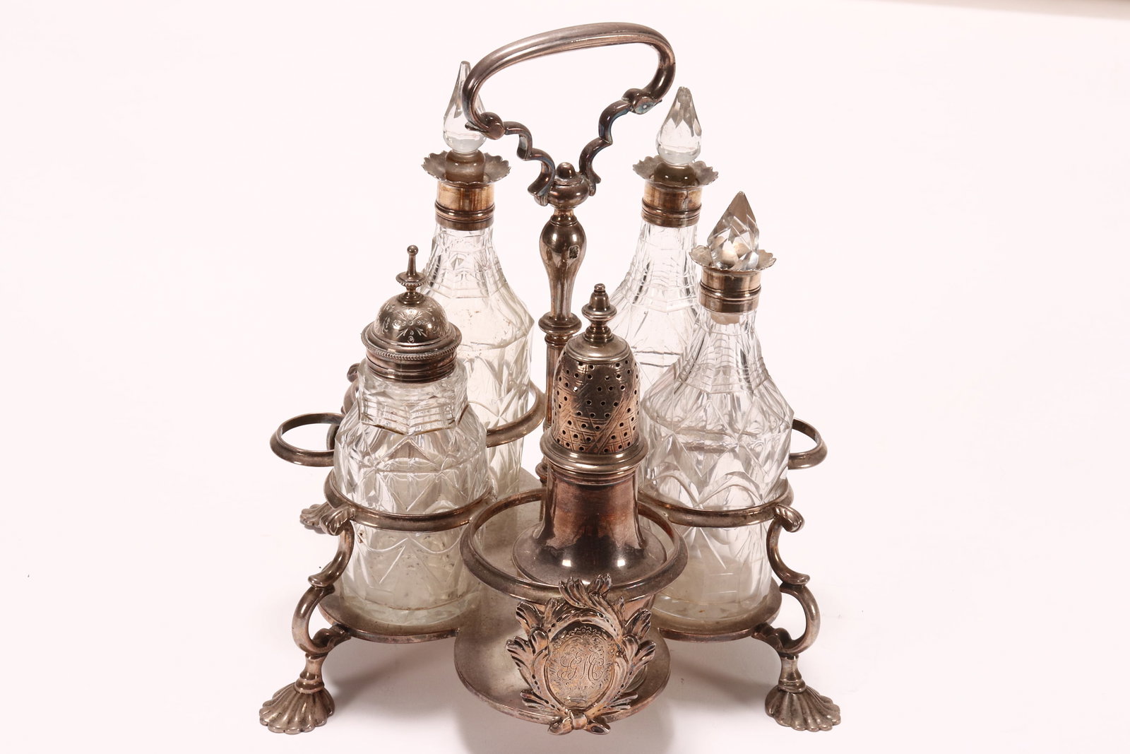 George II Sterling Silver and Crystal Cruet Set,: hallmarked London, 1739, SW (Samuel Wood), of cinquefoil form, with tall central handle, and acanthus reserve to support, raised above four shell form feet, the stand housing three cut crystal bottles