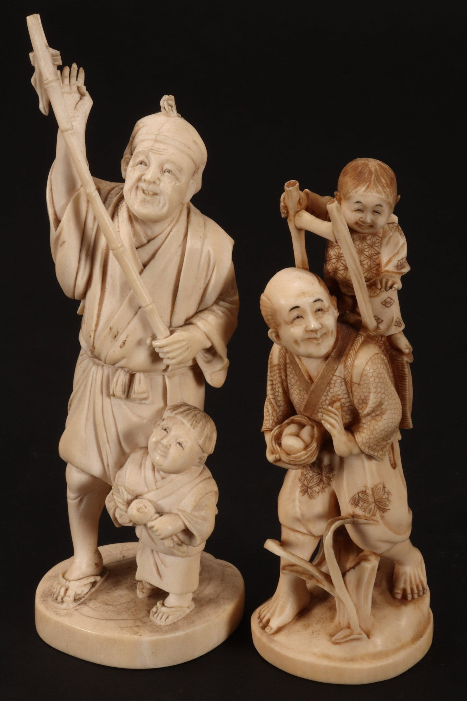 Two Japanese Carved Figures,: each depicting a man and young child, signed to base, height 15cm and 18cm (2) Please note this item can only be shipped WITHIN Australia.