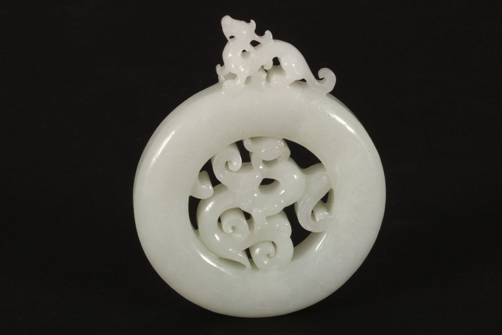 Chinese White Jade Carving,: of bi disc form, set with a pierced dragon finial, above continuously incised Archaic style mythical creatures to body, diameter 8cm