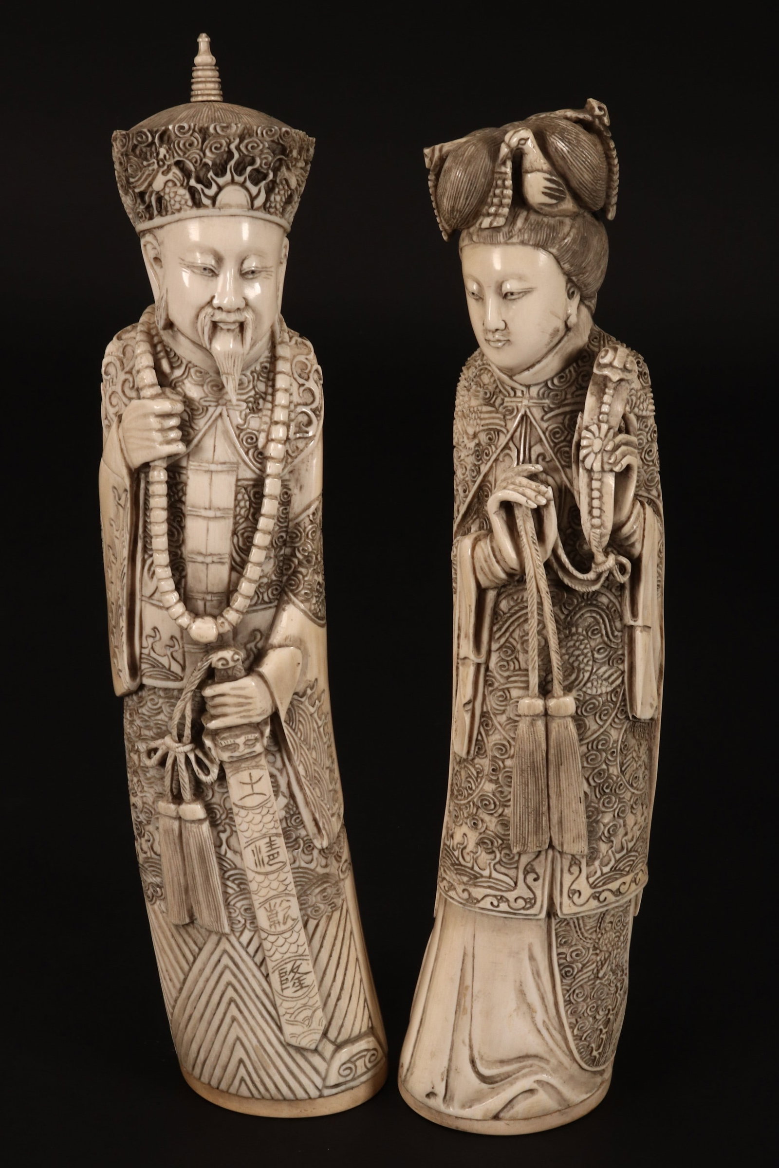 Large Pair of Chinese Emperor and Empress Figures,: the emperor depicted wearing a dragon robe and crown, holding beads in one hand and clasping a sword in the other hand, the empress depicted in a peacock robe holding a ruyi in her hands, marks to bas