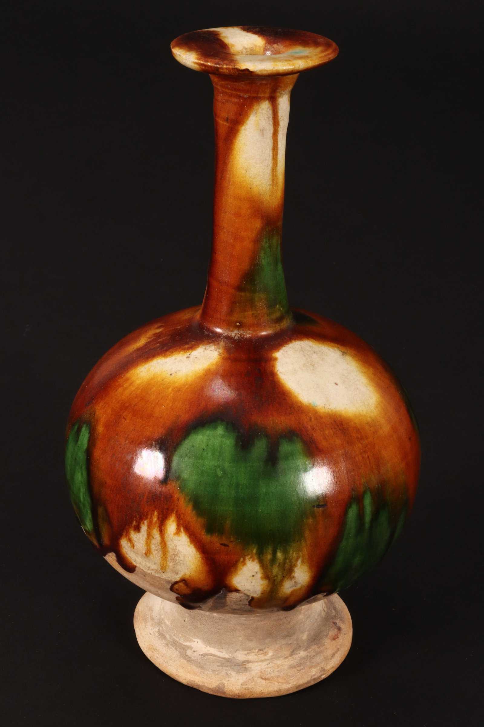 Chinese Sancai Glaze Ceramic Vase,: of bottle form, decorated with splashes of colour to body, neck and rim, in tones of brown, green and white, standing on a pedestal foot, height 21cm