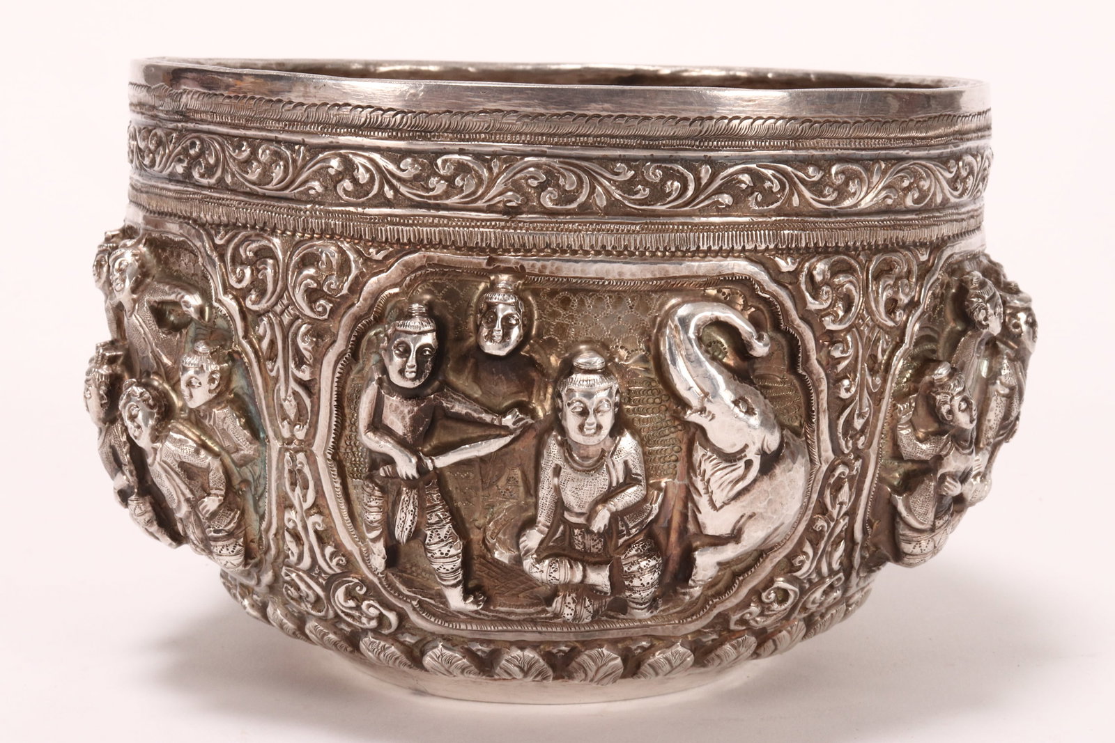 Burmese Silver Bowl,: of bulbous form, decorated in high relief with repousse panels depicting figures in various scenes, with acanthus accents, total weight 358g, height 9.5cm and diameter 15cm Provenance: The John Wolfe,