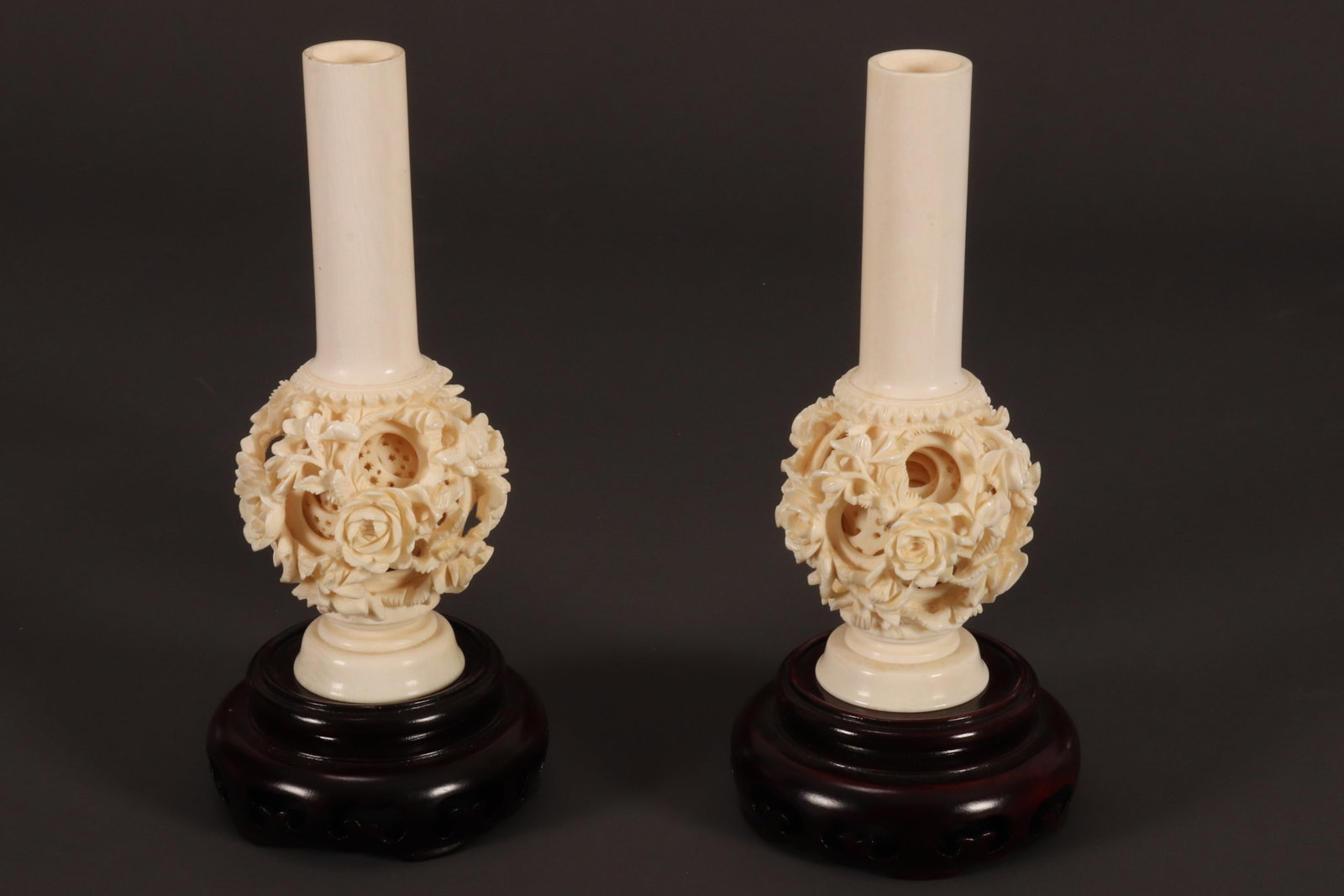 Pair of Chinese Puzzle Ball Vases,: with plainly decorated cylindrical neck, set above a pierced spherical puzzle ball, raised on a stepped circular foot, height 14cm, together with pierced timber stand (2). Please note this item can on