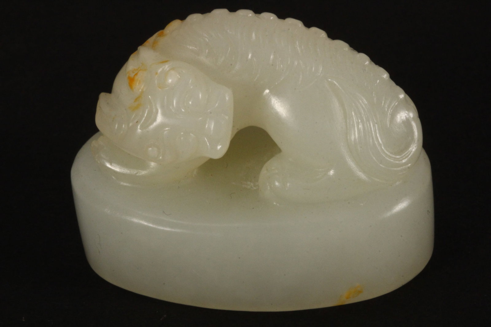 Chinese Carved White Jade Figural Seal,: depicting a fo dog seated on all four legs, raised on an oval base, with incised seal, in white tones with russet skin, height 3cm and length 4.5cm