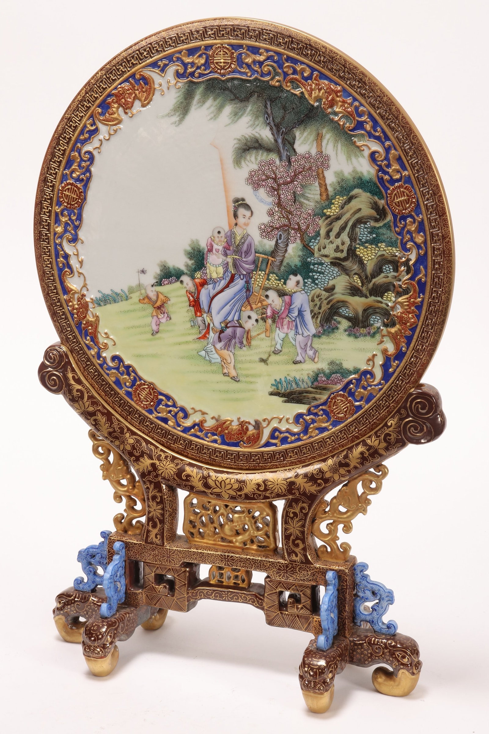 Chinese Porcelain Panel and Stand,: the panel of circular form, decorated with a central scene depicting a woman with six children in an outdoor setting, with a border of bats, symbols and scrolling foliage, raised on a pierced stand, d