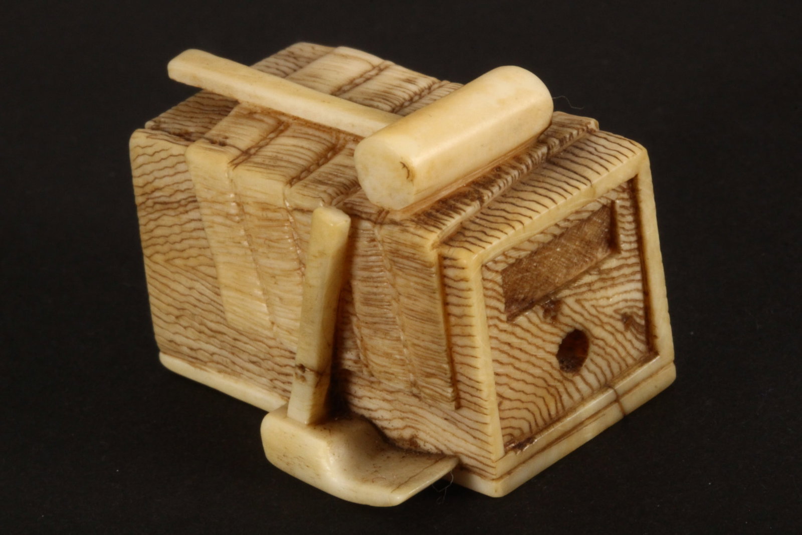 Japanese Carved Netsuke,: depicting a tool chest, with mallet and hoe, the box with delicately incised and stained wood grain detail, unsigned, length 3.2cm. Please note this item can only be shipped WITHIN Australia.