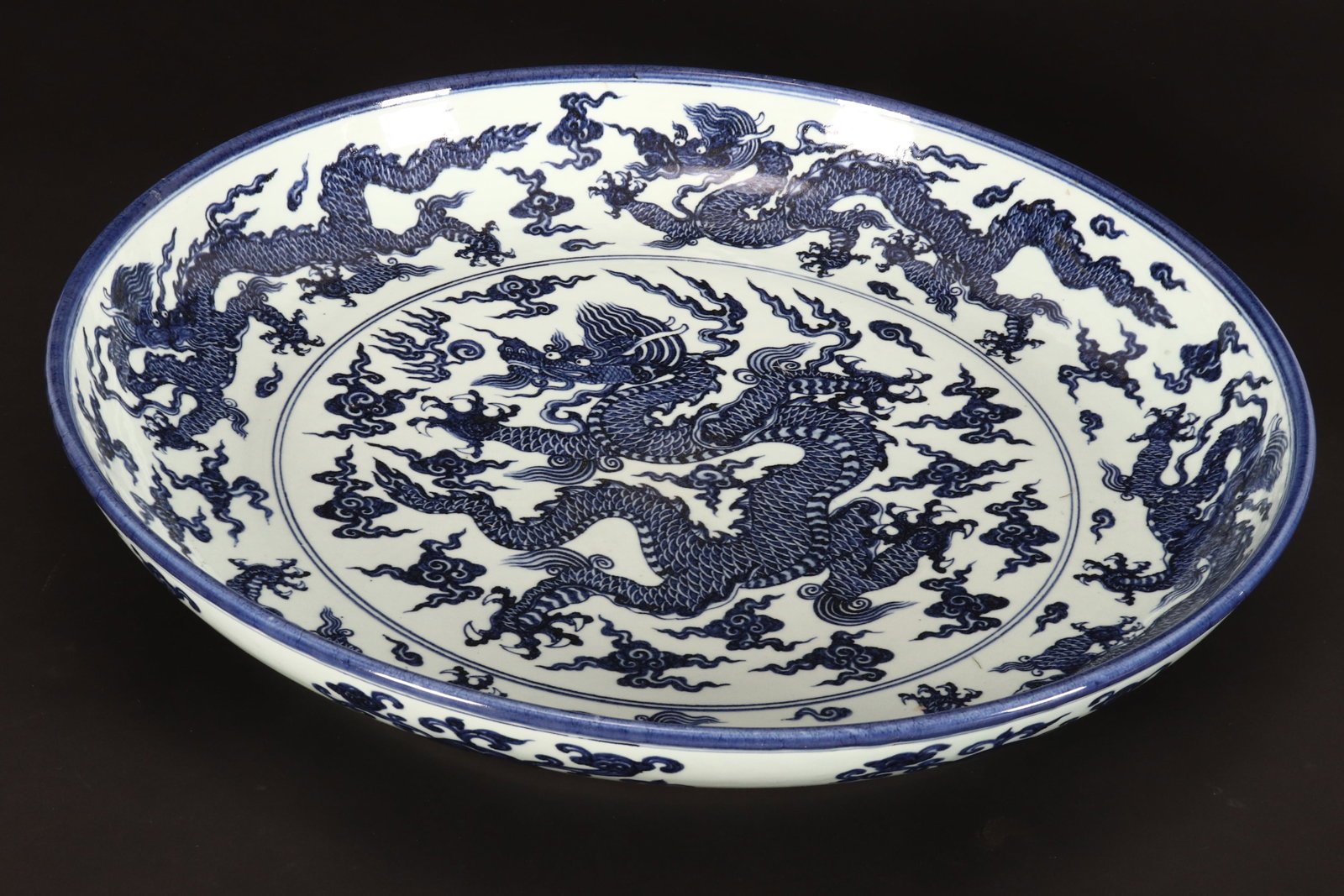 Large Chinese Blue and White Porcelain Charger,: of circular form with flared rim, the interior decorated with central roundel of a dragon amongst stylised clouds, surrounded by multiple dragons and stylised clouds, the exterior decorated with ruyi 