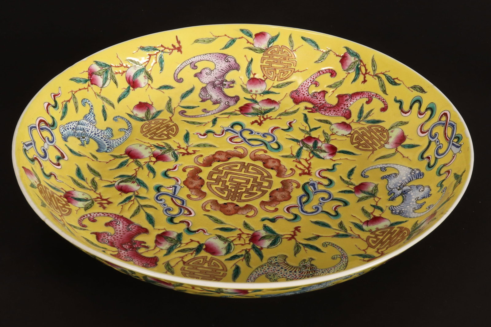 Chinese Famille Jaune Porcelain Dish,: of shallow circular form, decorated continuously with shou symbols, bats, peaches, ruyi heads and foliage, in tones of pink, orange, green and blue on a yellow ground, accented with gilt, standing on 
