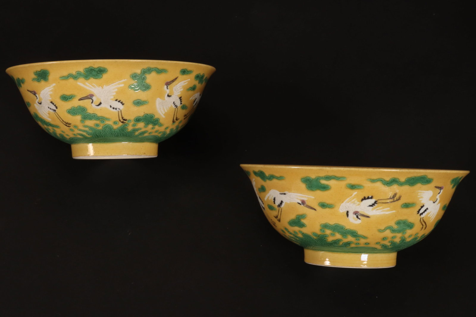 Pair of Chinese Famille Jaune Crane Bowls,: of conventional form, decorated with continuous scene of eight cranes flying amongst stylised clouds and above turbulent waves, in tones of green, white, pink and black on a yellow ground, standing on