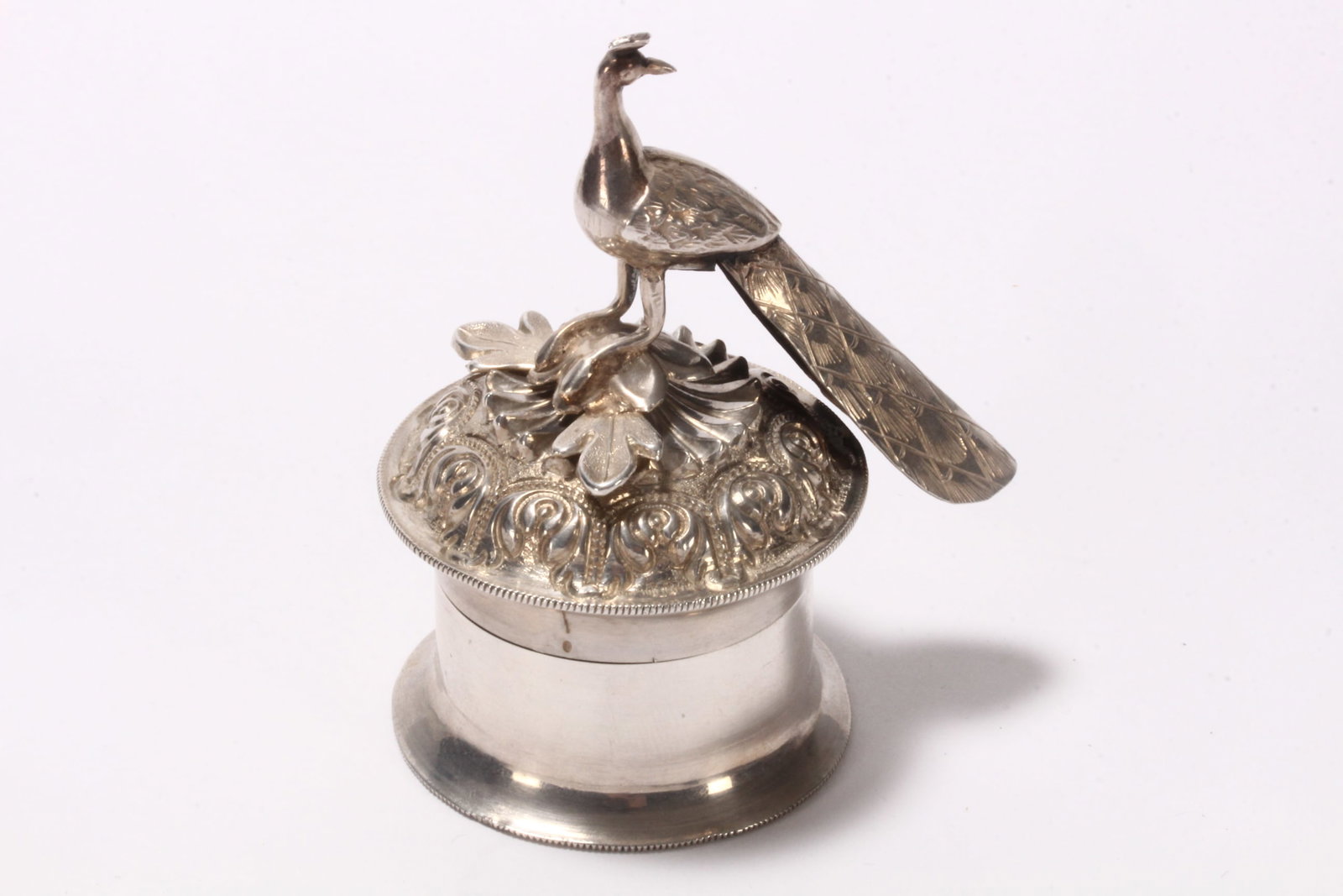 Indian Silver Sindoor Dabbi,: unmarked (acid tested silver), of cylindrical form, the domed cover set with peacock finial, perched above a blossoming flower, opening to reveal a smaller container within, housing a vial of vermilio