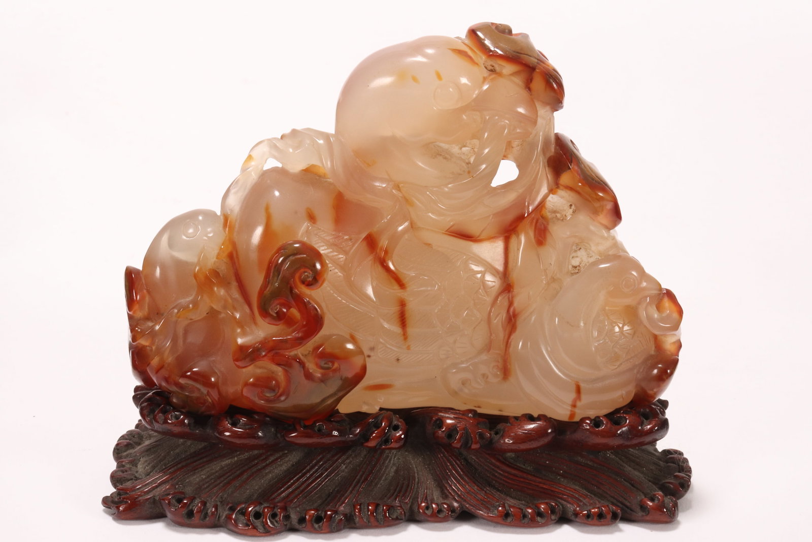Chinese Carved Agate Figure Group on Stand,: depicting seated bird flanked by chicks holding lingzhi in beaks, the birds surrounded by fruit and foliage, in tones of white, orange and brown with russet skin, raised on an organic form carved wood