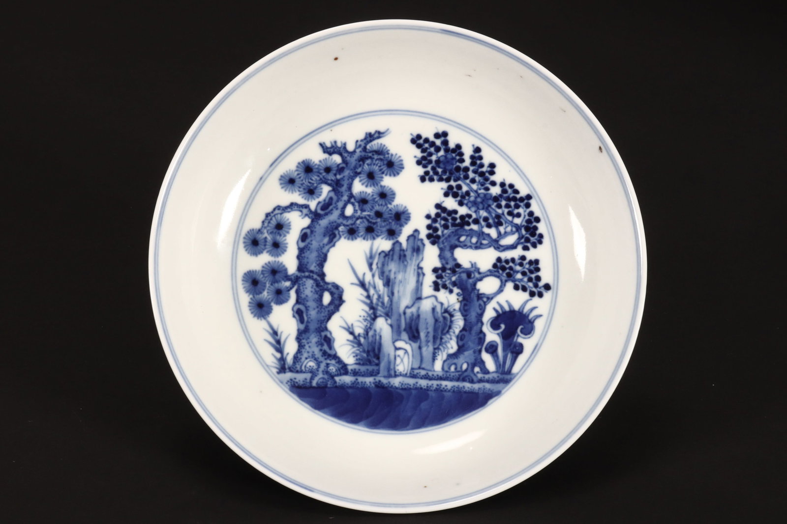 Chinese Blue and White Porcelain Bowl,: of shallow circular form, decorated to interior with roundel depicting pine tree, prunus, rocky outcrop and lingzhi, the exterior decorated with figures in a pavillion, six character mark to base, hei