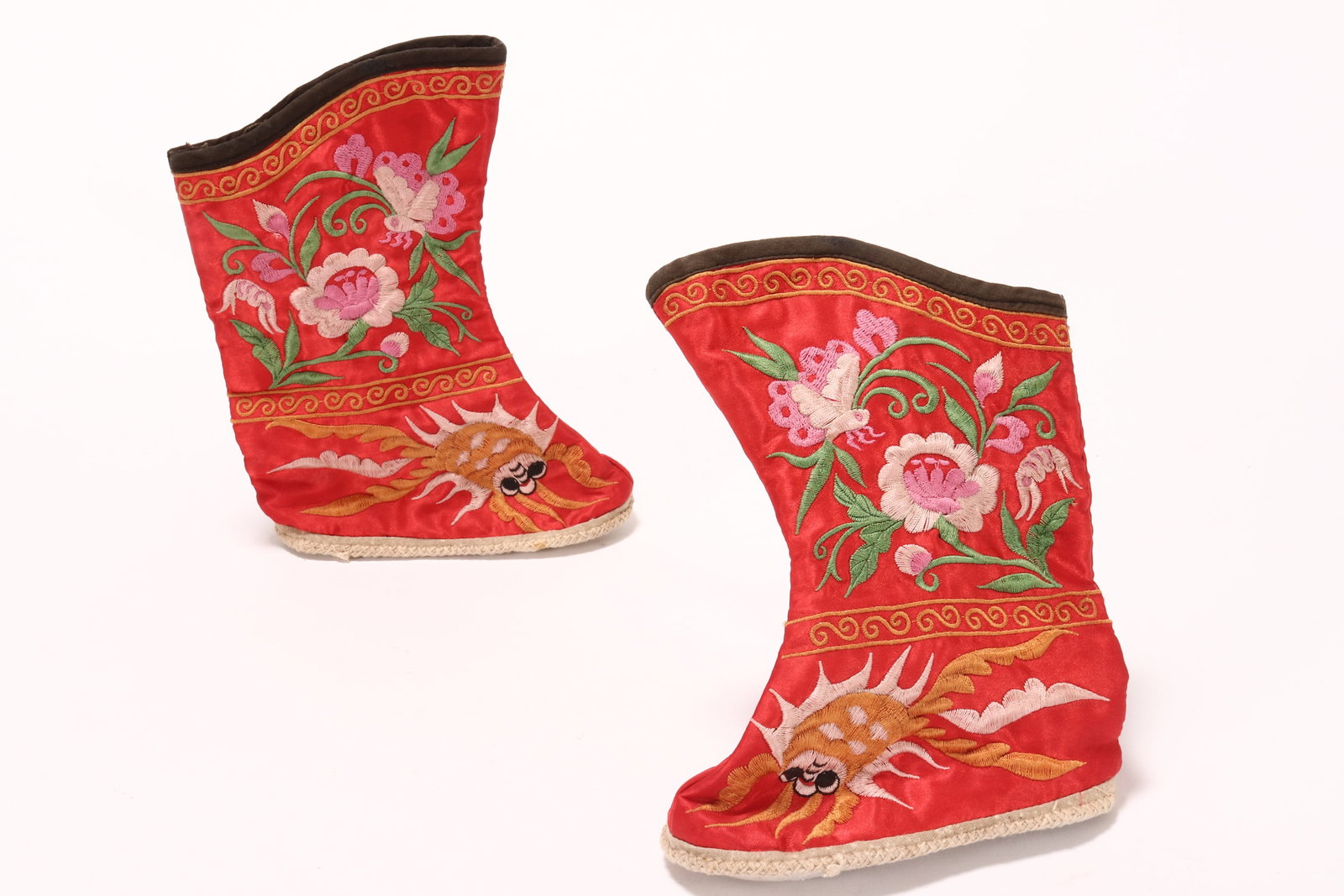 Pair of Chinese Children's Silk Boots,: of conventional form, decorated with embroidered peonies, butterflies and goldfish, in tones of pink, green and yellow on a red ground, with white cotton soles, height 18.5cm and length 13.5cm