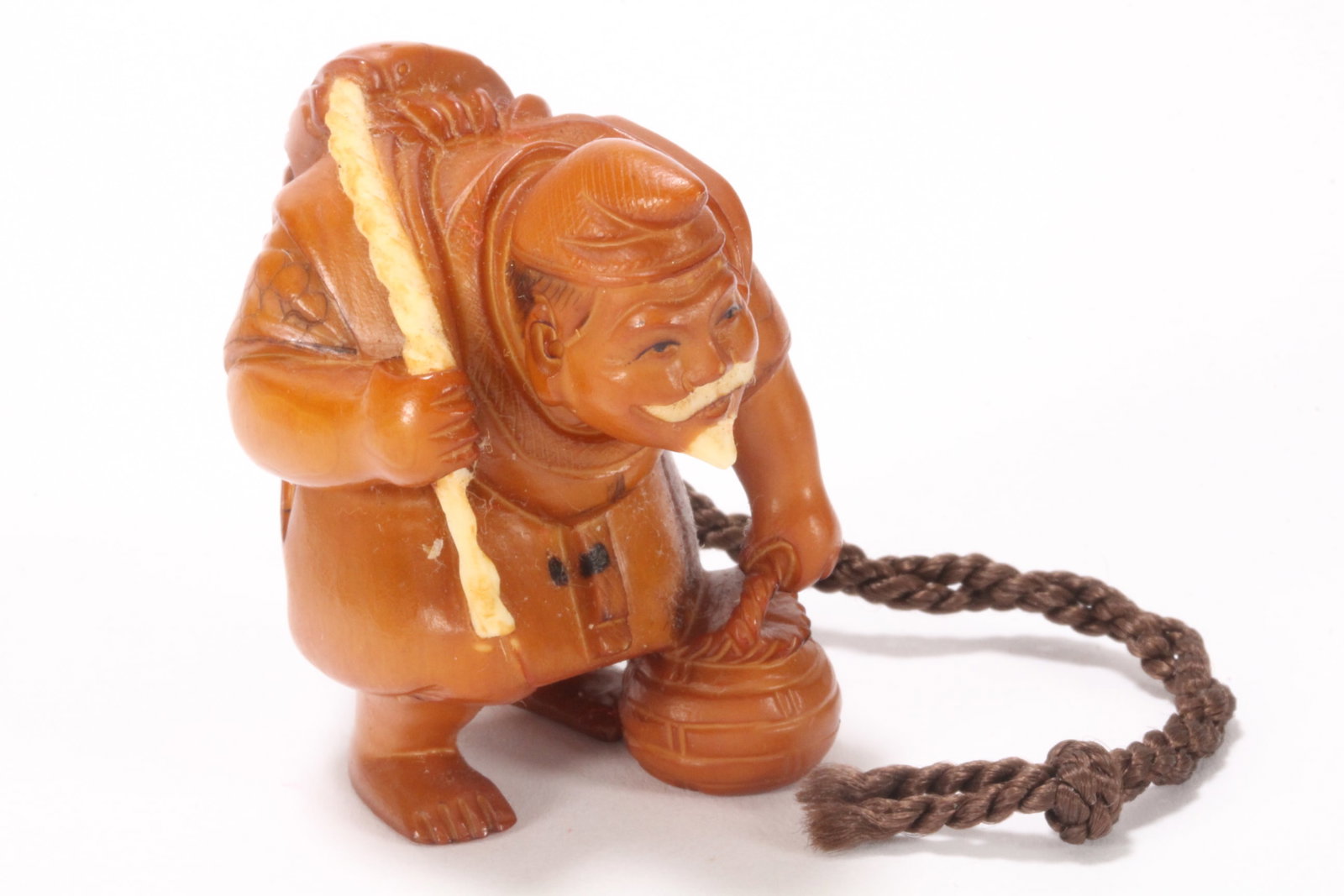 Japanese Carved Netsuke,: in the form of a hunched fishermen, carrying a basket in one hand, with a fish suspended by a rope over his shoulder, with incised detail and staining, two character mark to base, height 4.6cm. Please