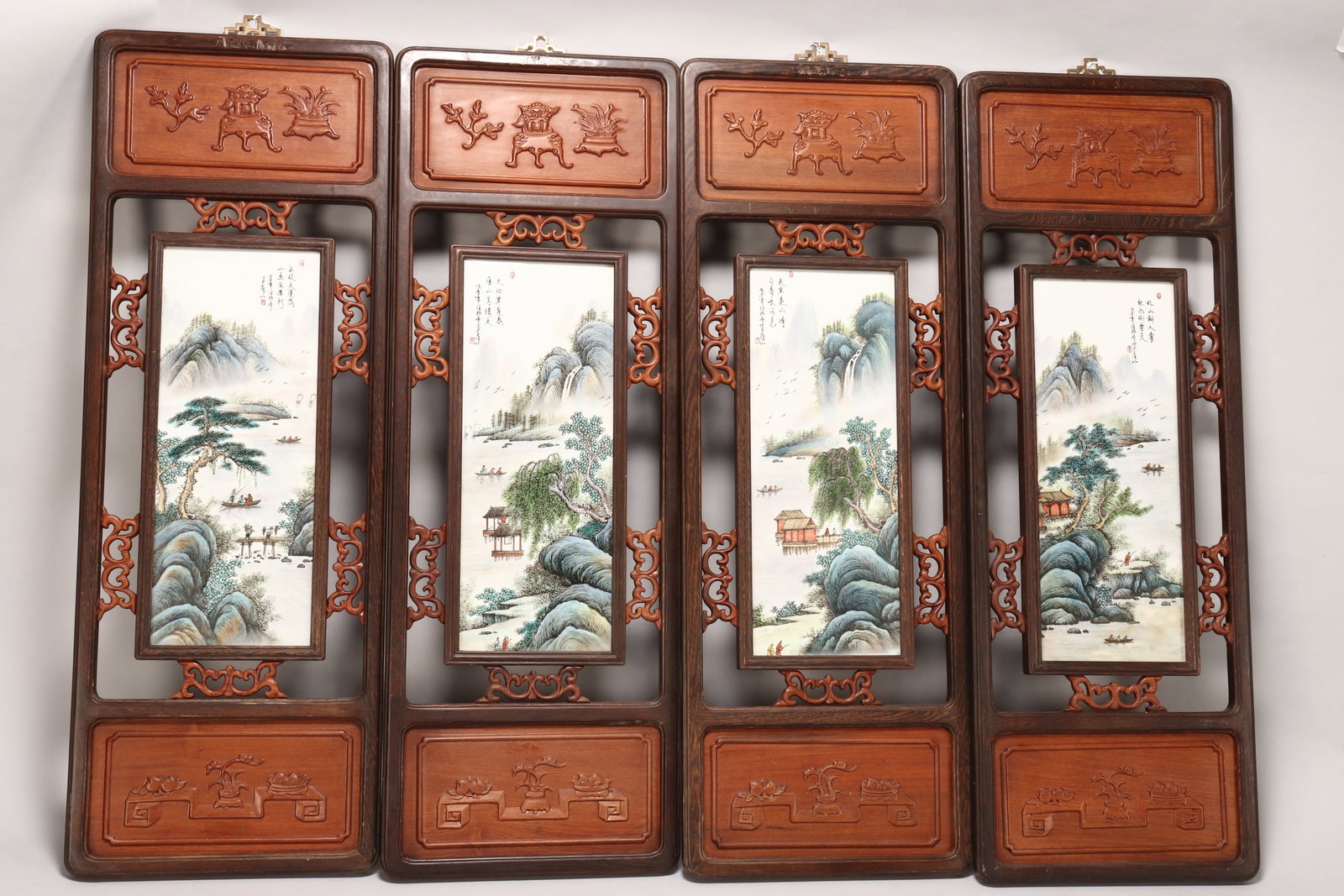 Set of Four Chinese Framed Porcelain Panels,: of rectangular form, all depicting a mountainous landscape with lake, boats, figures and birds, with script and seal marks to upper right and left, set within a carved and pierced wooden frame, 41.5cm