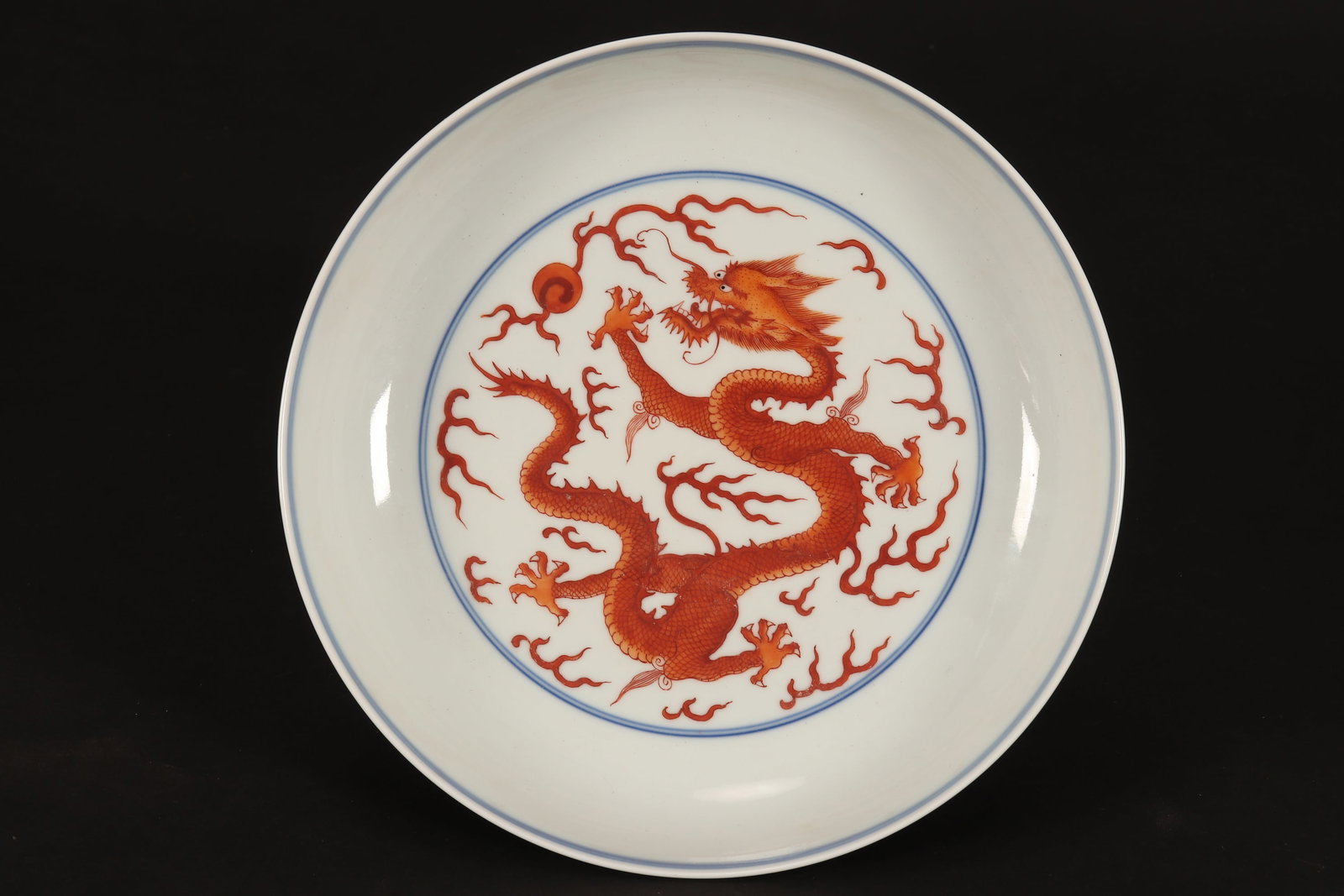 Chinese Blue, White and Iron Red Porcelain Dish,: of circular form, decorated with central roundel depicting a dragon pursuing flaming pearl amongst stylised clouds, the exterior decorated with a continuous scene of two dragons pursuing flaming pearl