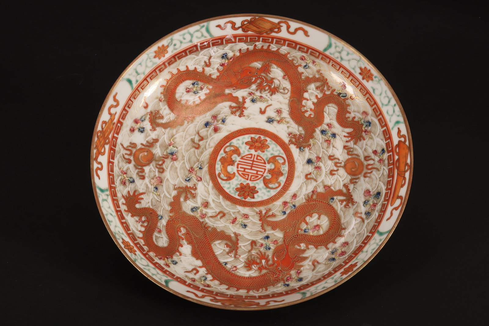 Chinese Porcelain Dish,: of shallow conventional form, the well decorated densely with central medallion housing a shou symbol, lotus and bats, encircled by two dragons in pursuit of the flaming pearl, with auspicious objects
