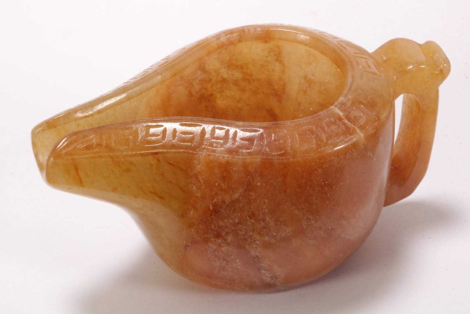Chinese Carved Jade Water Pourer,: of cylindrical form with flared spout and stylised handle, decorated with Greek key border to rim, in tones of white, orange and brown, height 4cm and length 8cm