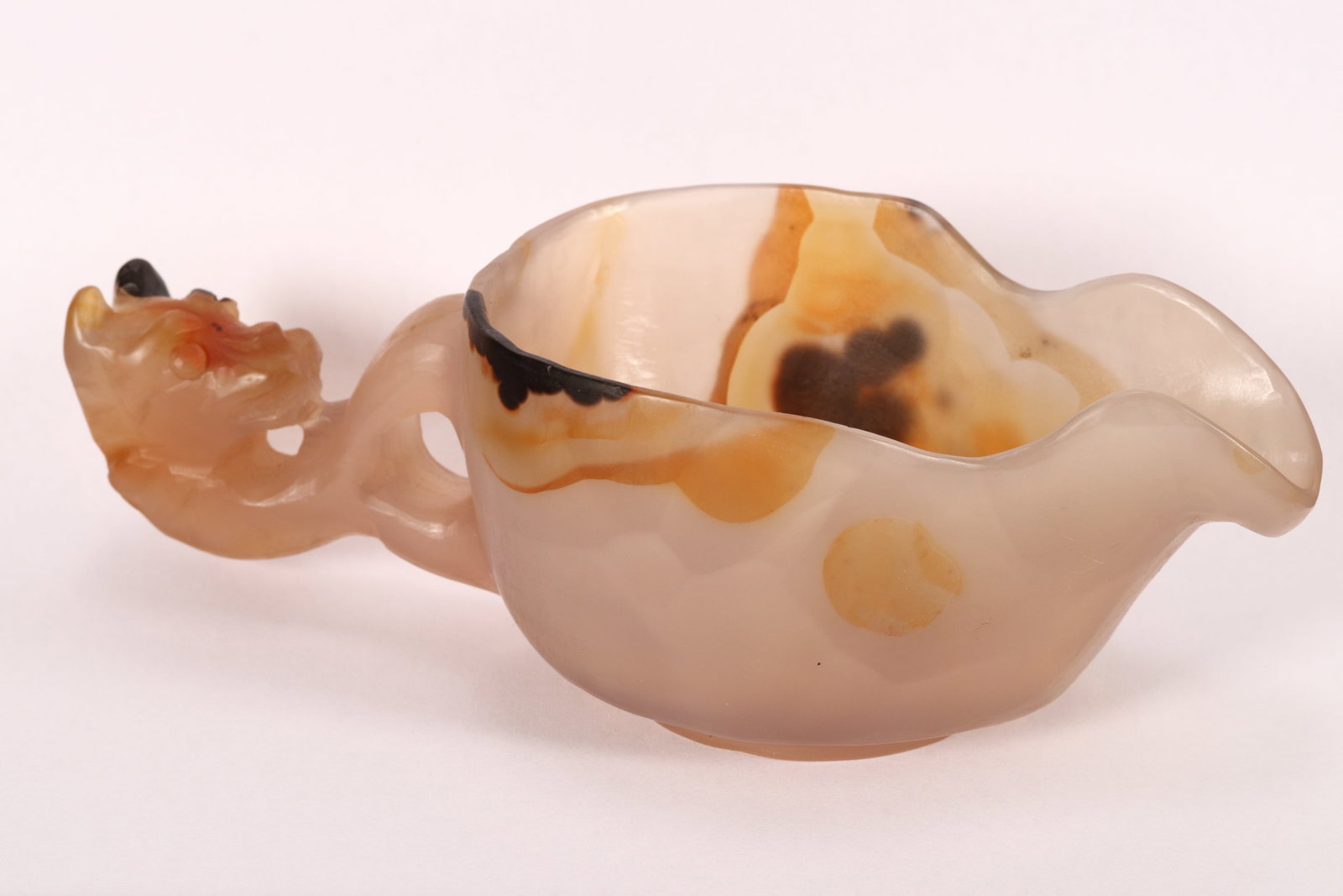 Chinese Carved Agate Libation Cup,: of shallow form with a wide spout, with carved figural handle, in pale tones with brown accents, raised on a short circular foot, height 5cm and 16cm