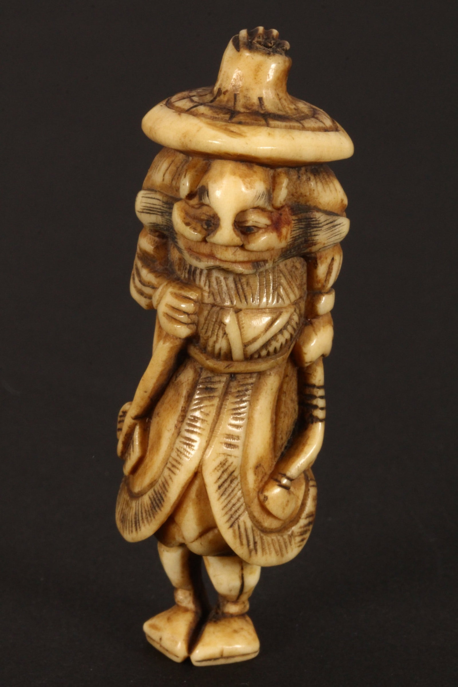 Japanese Edo Period Stag Antler Netsuke,: in the form of a figure, depicted in a wide brimmed hat and long coat, holding a bow in one arm and arrow in the other, height 7.5cm and width 2.5cm