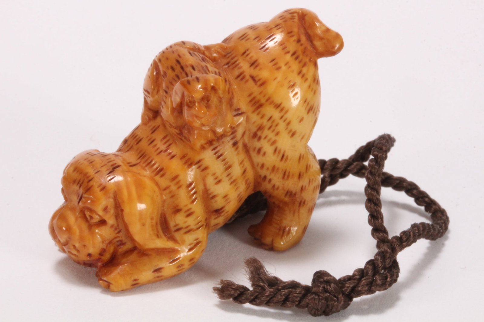 Japanese Carved Netsuke,: depicting a dog bowing, with puppy on its back, each figure with incised hairwork and staining, signed to base, length 4.3cm. Please note this item can only be shipped WITHIN Australia.