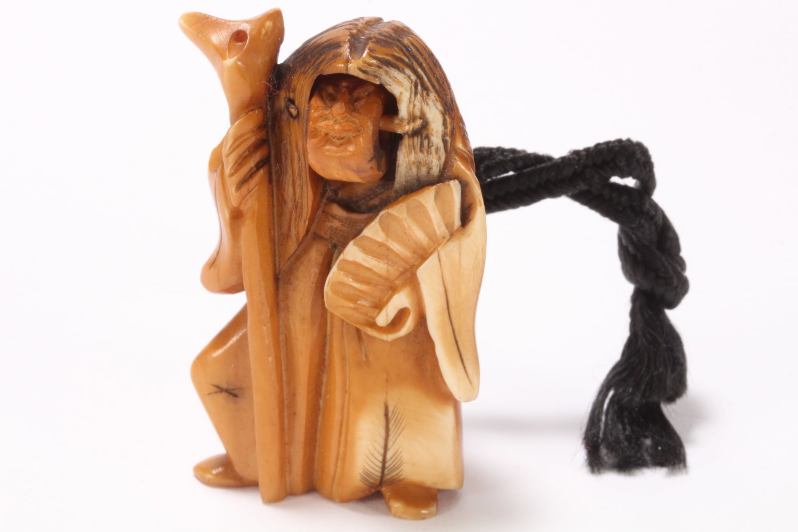 Japanese Carved Netsuke,: in the form of a Kabuki actor, with rotating Noh mask, the figure depicted grasping a staff in one hand, and an open fan in the other, with incised detail to the hair and robes and stained accents, in