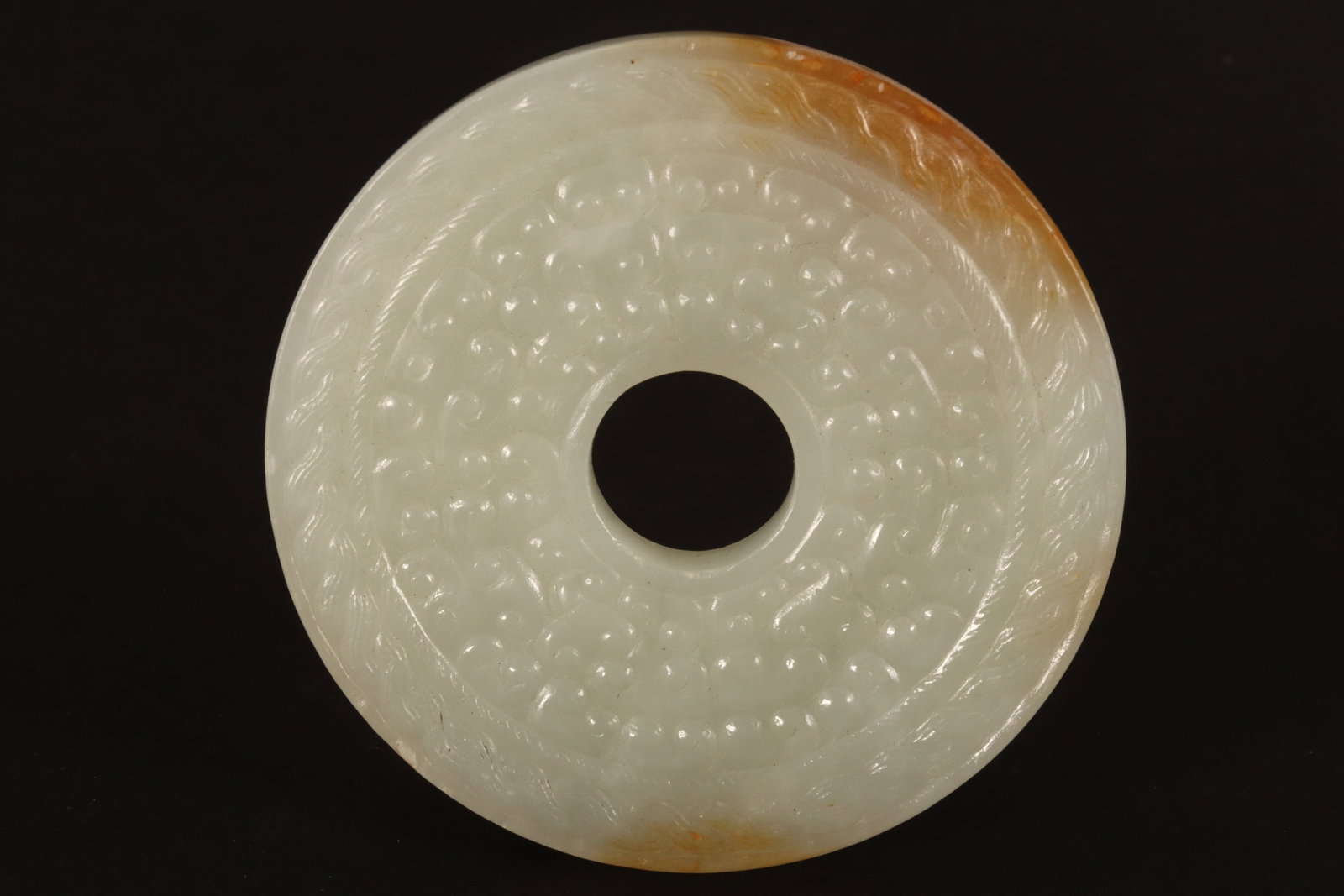 Chinese White Jade Bi Disc,: of circular form, decorated with scroll motifs in relief surrounded by rope, in white tones with russet skin, diameter 6cm