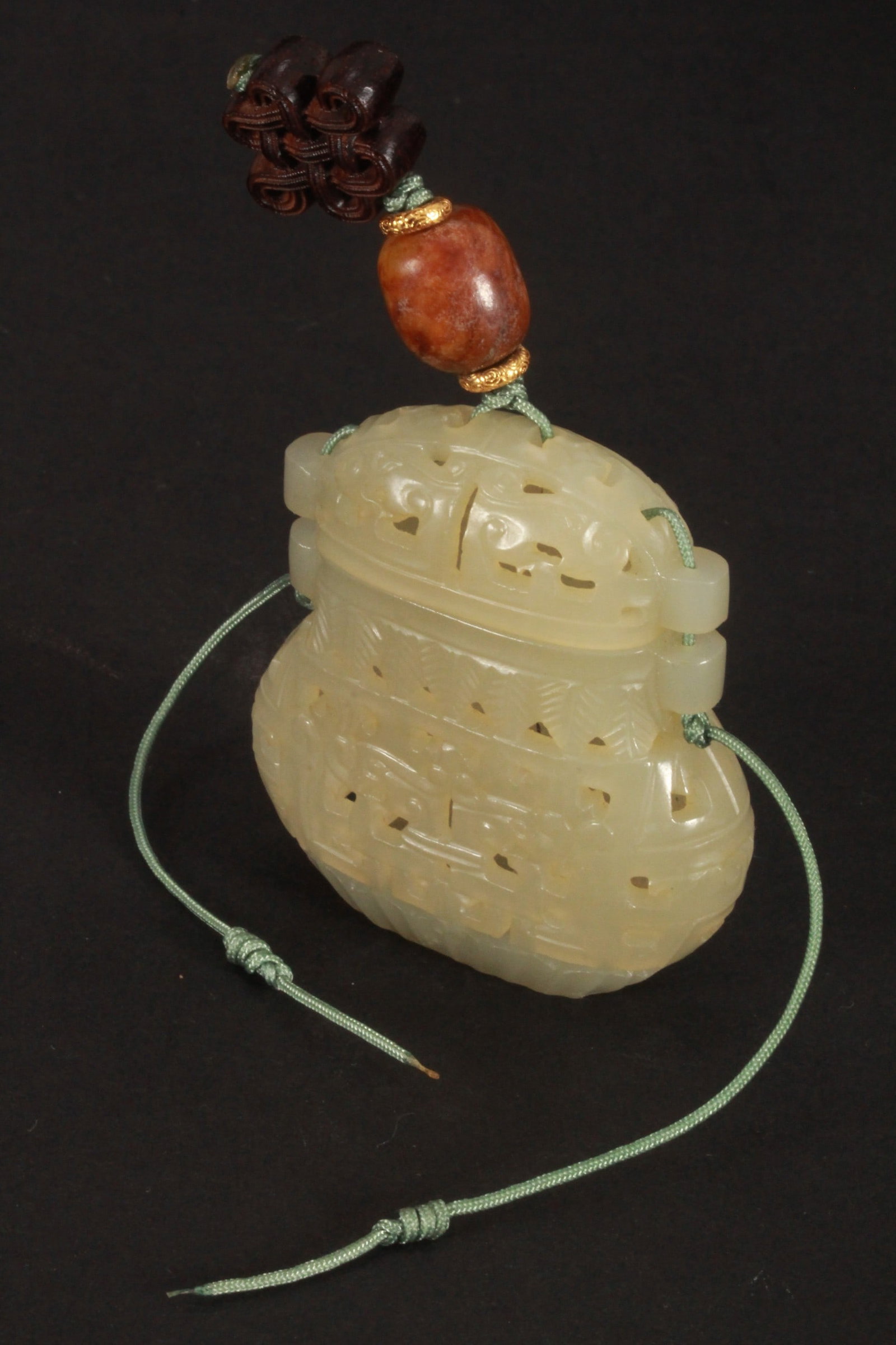 Chinese Carved Jade Incense Pouch,: in the form of a pierced vase, decorated with Taotie mask design, flanked by decorative borders, in tones of pale green, suspended on a braided cord, accented with timber beads, length 8.5cm