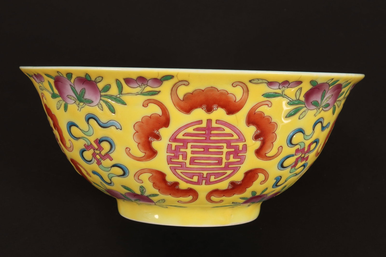 Chinese Famille Jaune Porcelain Bowl,: of tapering circular form, decorated with shou symbol surrounded by bats alternating with ribbon, peaches and foliage, in tones of orange, red, pink and green on a yellow ground, standing on a raised 