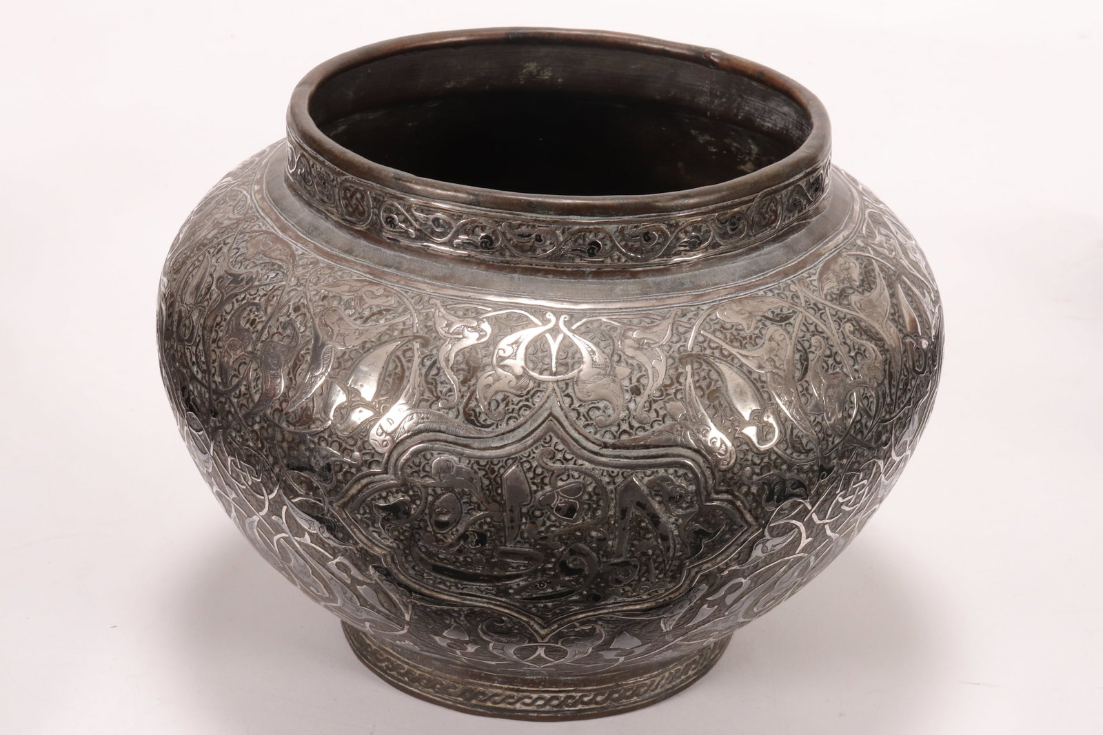 Late 19th Century Persian Silver Overlay Copper: Bowl, of tapering form, the body decorated profusely with shaped reserves housing Islamic script, on a ground of scrolled foliates, the whole raised above a circular foot, height 16.5cm