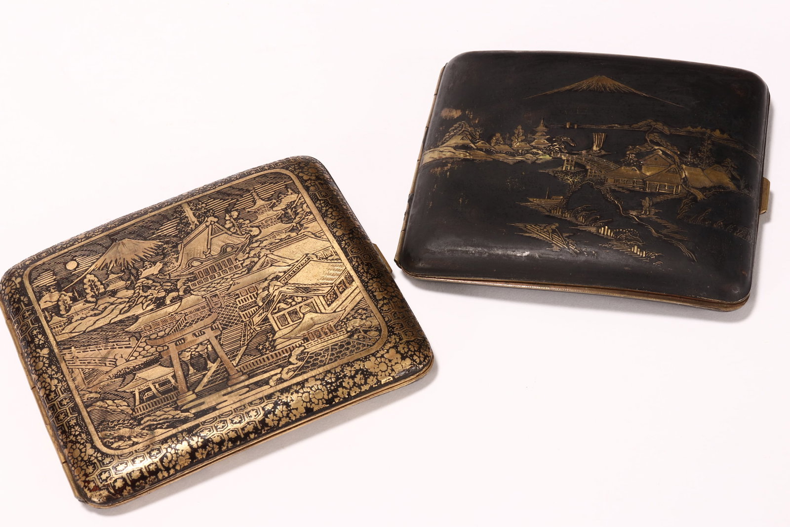 Two Japanese Damascene Cigarette Cases,: each of rectangular form, the larger intricately decorated with reserves containing a mountainous village scene, with two dragons in flight, each scene with a distant Mount Fuji visible behind, 8cm x 