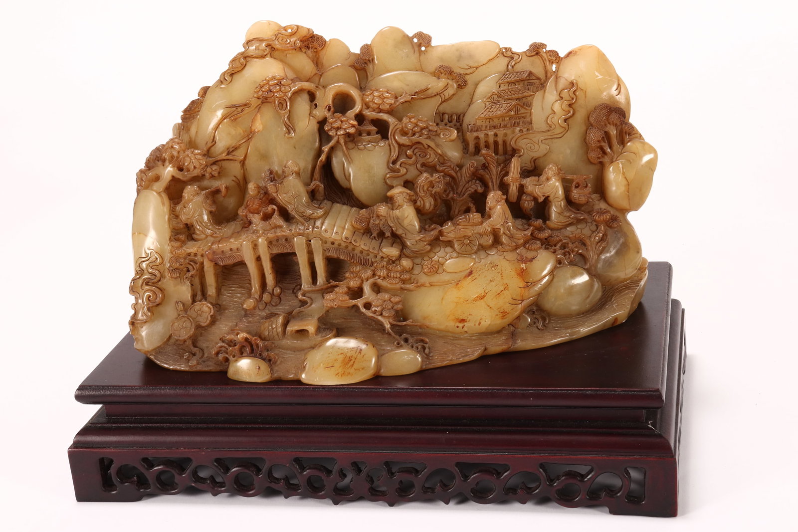 Chinese Carved Stone Boulder,: depicting a hillside village scene, with traversing merchant figures, in tones of green and brown, height 18.5cm and length 30.5cm, together with a pierced timber stand