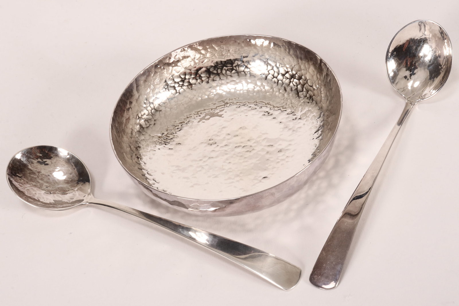 Three Zimbabwean Pure Silver Items,: hallmarked AG 999 (Argentum Silversmiths, Harare), Edward, comprising a bowl, of shallow form with a hand beaten finish, diameter 10.5cm, together with two spoons, length 14.5cm and 14cm, total weight