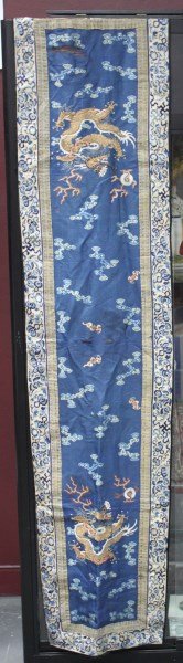 Chinese Late Qing Dynasty Embroidered Table: Runner, embroidered with gold thread rampant dragons chasing flaming pearls surrounded by bats and clouds, with a brocade and floral border in tones of blue, a/f, 178 x 41cm