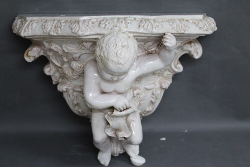 Large Maiolica Figural Bracket,: with a shaped pediment supported on the back of putto surrounded by acanthus scrolls,in a white glaze, h 38cm